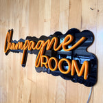 LED-neonskilt «ChampagneROOM» oransje neonlys på sort skiltform.