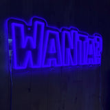 LED-neonskilt med teksten WANTA? i blått, med synlige tilkoblingskabler.