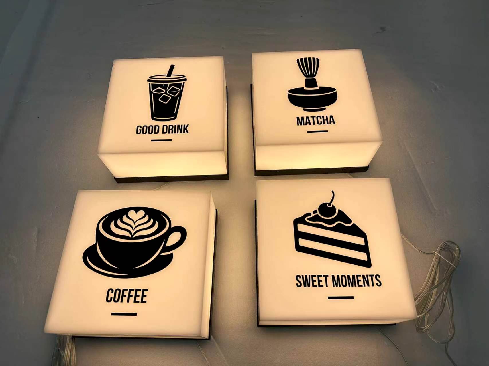Veggkube med logo: fire kvadratiske lysbokser med kaffe-, matcha- og kakeikoner